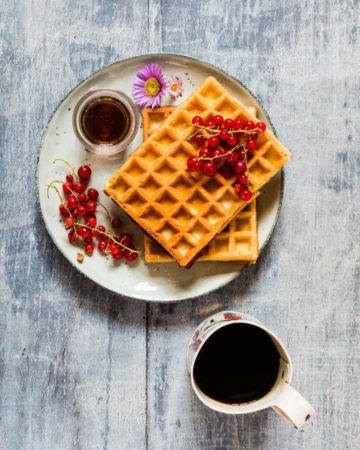 overhead shot of honey waffles on a plate with blue rim next to a cup of coffee