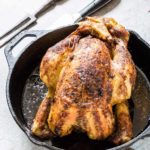 Roast nutmeg orange chicken recipe in a skillet with carving utensils next to it