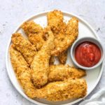 cooked air fryer chicken tenders on a white plate and served with a ramekin filled with ketchup