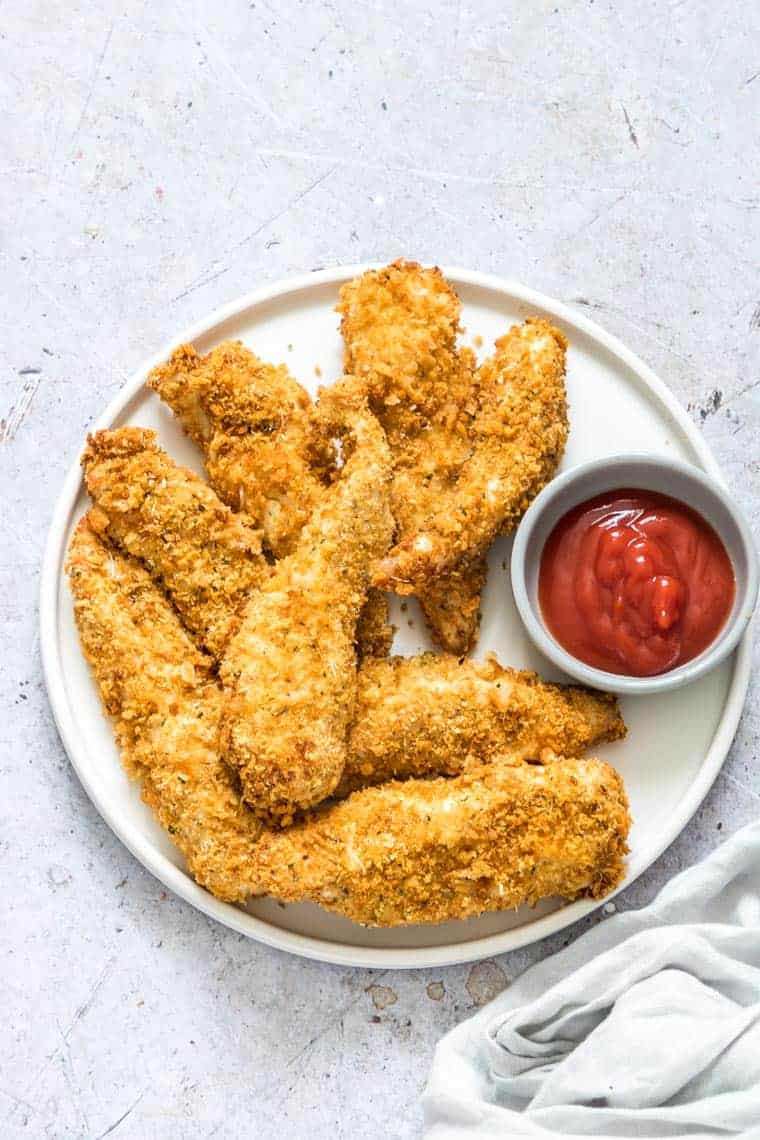 cooked air fryer chicken tenders on a white plate and served with a ramekin filled with ketchup