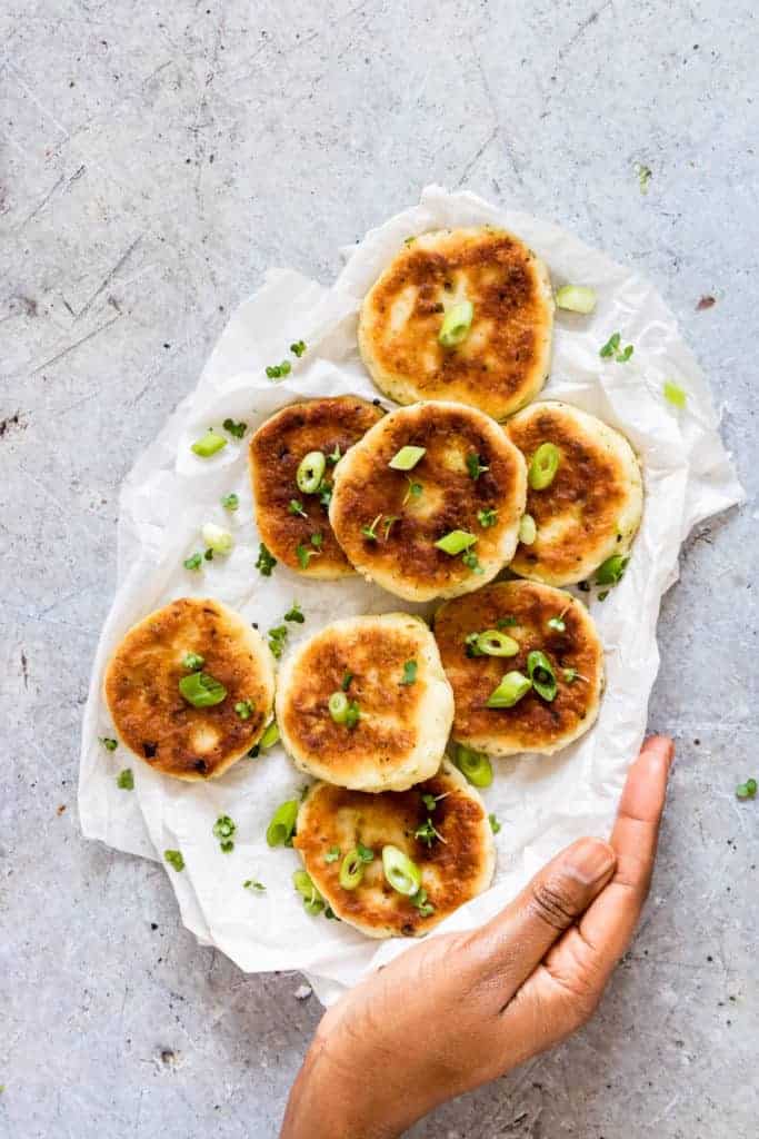 8 Potato Pancakes with Leftover Mashed Potatoes on a white paper with spring onions, cress and a dip with a hand holding them
