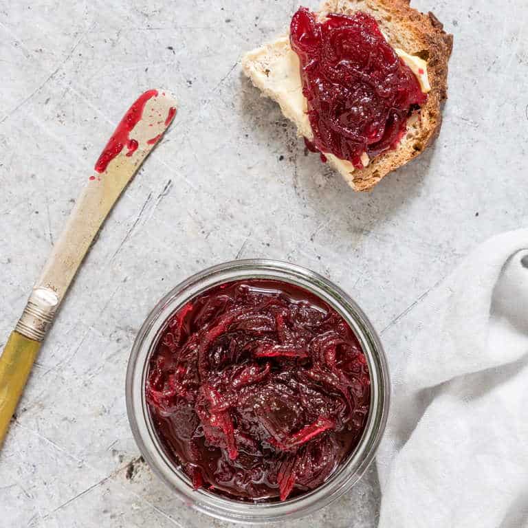 beetroot relish on table next to knife with relish and bread with relish