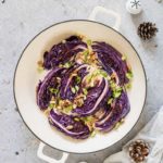 Roasted red cabbage in a pot with walnuts, spring onions, a spoon, a bowl of walnuts, cloth, pine cones