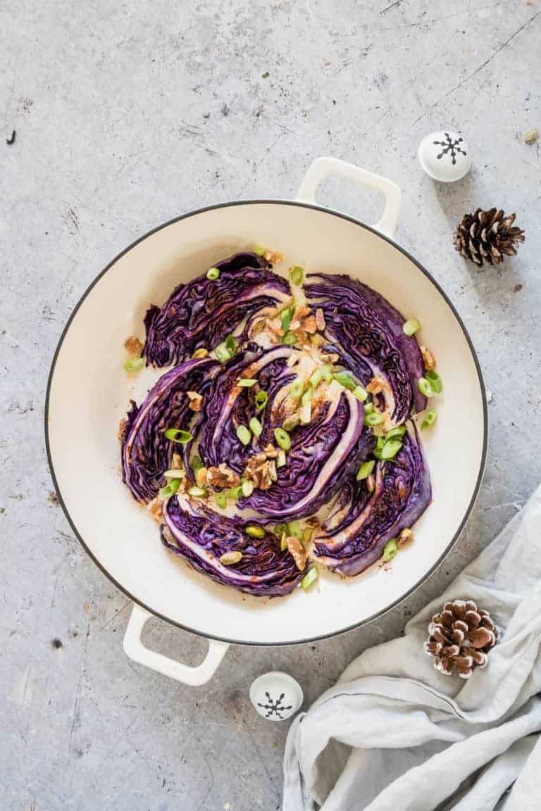 Roasted red cabbage in a pot with walnuts, spring onions, a spoon, a bowl of walnuts, cloth, pine cones