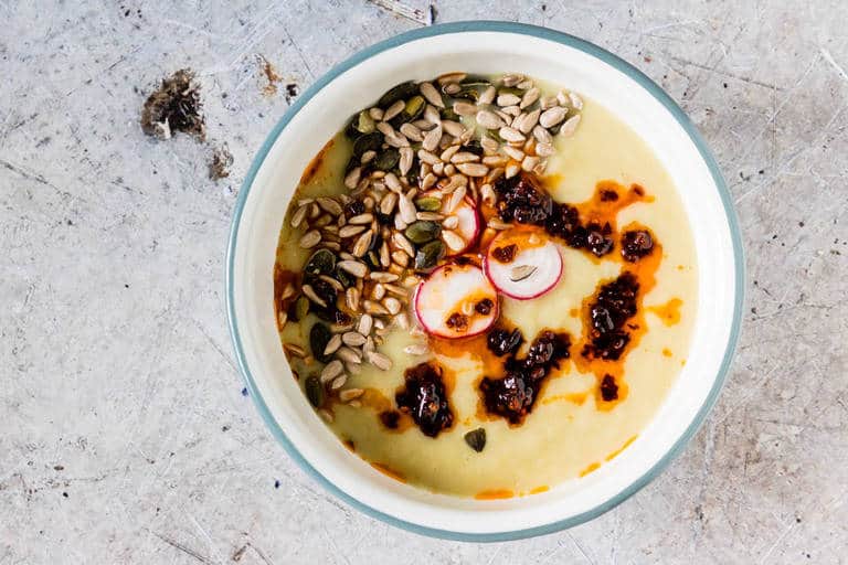 Instant Pot Potato Soup in a bowl, with pumpkin seeds, chili, and radishes shot from overhead.