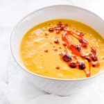 Over head shot of sweet potato and carrot soup in a white bowl with chilli oil