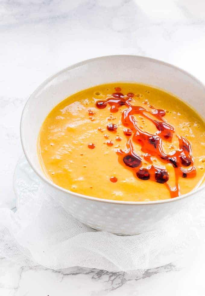 Over head shot of sweet potato and carrot soup in a white bowl with chilli oil