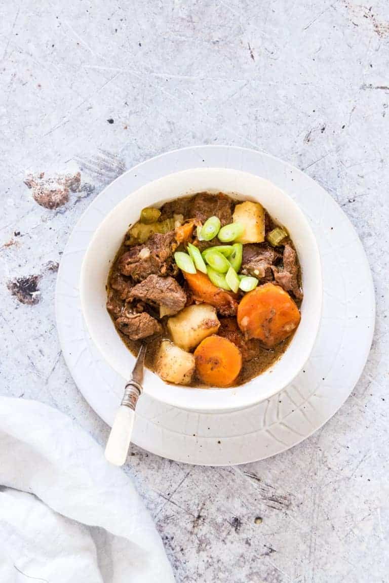 A bowl of Instant Pot Beef Stew on a plate with a spoon