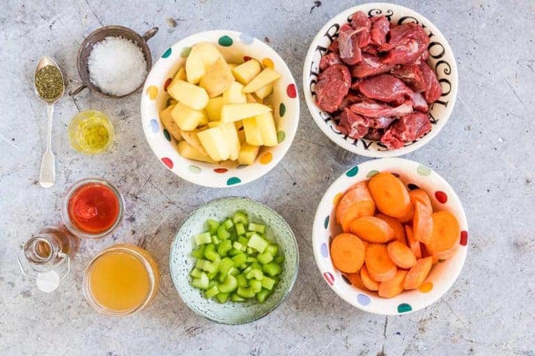 Ingredients For Instant Pot Beef Stew in various bowls on a table. - potatoes, carrots, beef, celery, oil, stock, tomatoes, herbs, salt, 