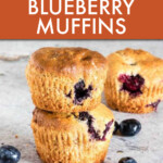 a stack of two blueberry muffins with blueberries scattered around them.