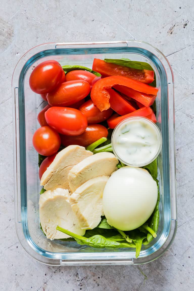 close up of a glass meal prep container filled with sliced Instant Pot Chicken Breast, tomatoes, red peppers, salad greens and a hard boiled egg 