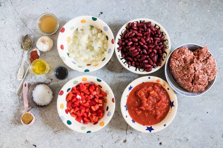 overhead view of ingredients to make Instant Pot Chilli – beef mince, onion, kidney beans, tomatoes, peppers, garlic, oil, herbs and salt and balsamic vinegar