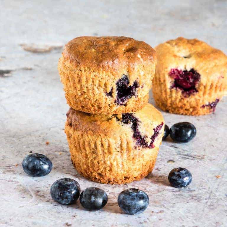 three vegan blueberry muffins surrounded by blueberries