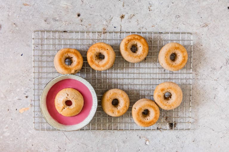 Donuts on a cooling rack with one donut dipped into a raspberry glaze