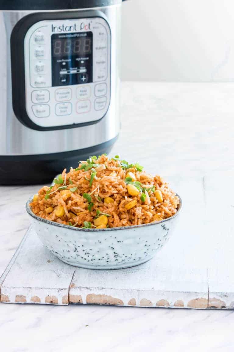 image of instant pot mexican rice in a bowl garnished with greens next to an instant pot
