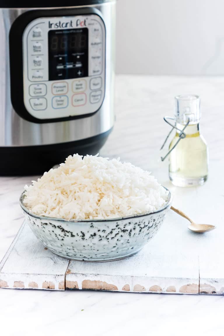 Bowl of instant pot white rice next to instant pot with seasoning and spoon