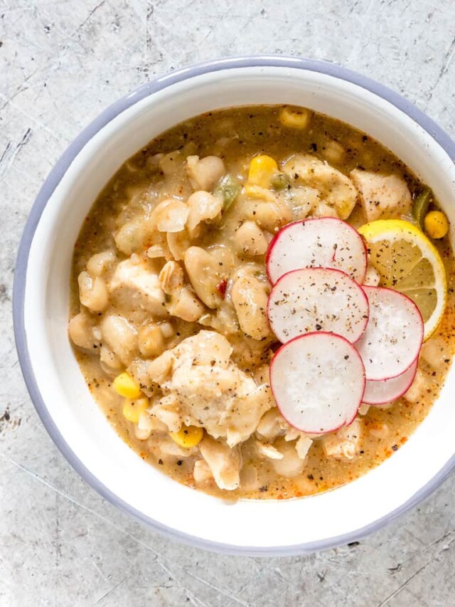 blue rimmed white bowl containing serving of white chicken chili with sliced radishes on top.