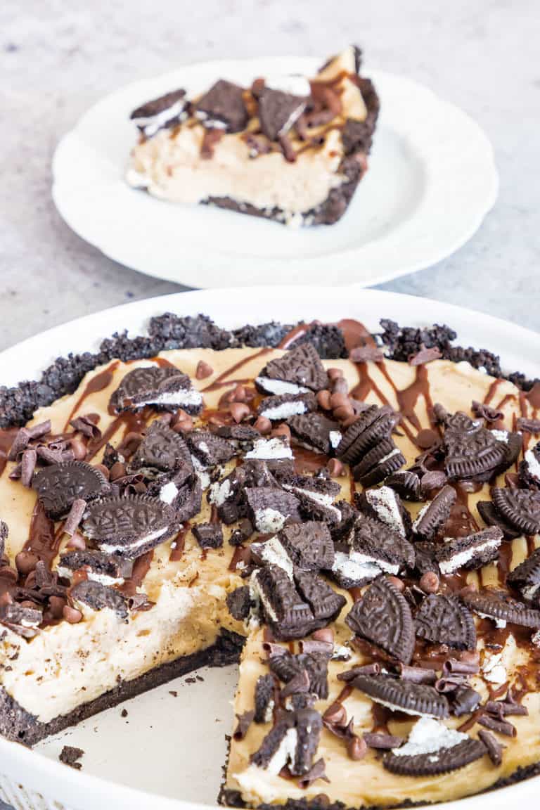 A peanut butter pie on a table topped with oreos and chocolate and sauce and a slice taken out