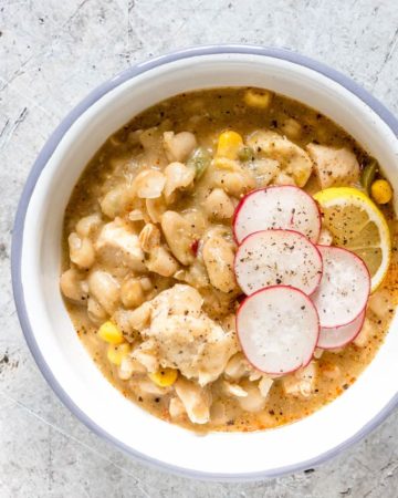 blue rimmed white bowl containing serving of white chicken chili with sliced radishes on top