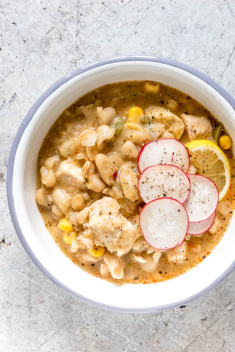 blue rimmed white bowl containing serving of white chicken chili with sliced radishes on top