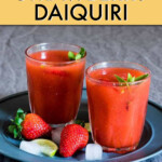 two strawberry daiquiris on a serving tray surrounded by ice cubes and fresh strawberries