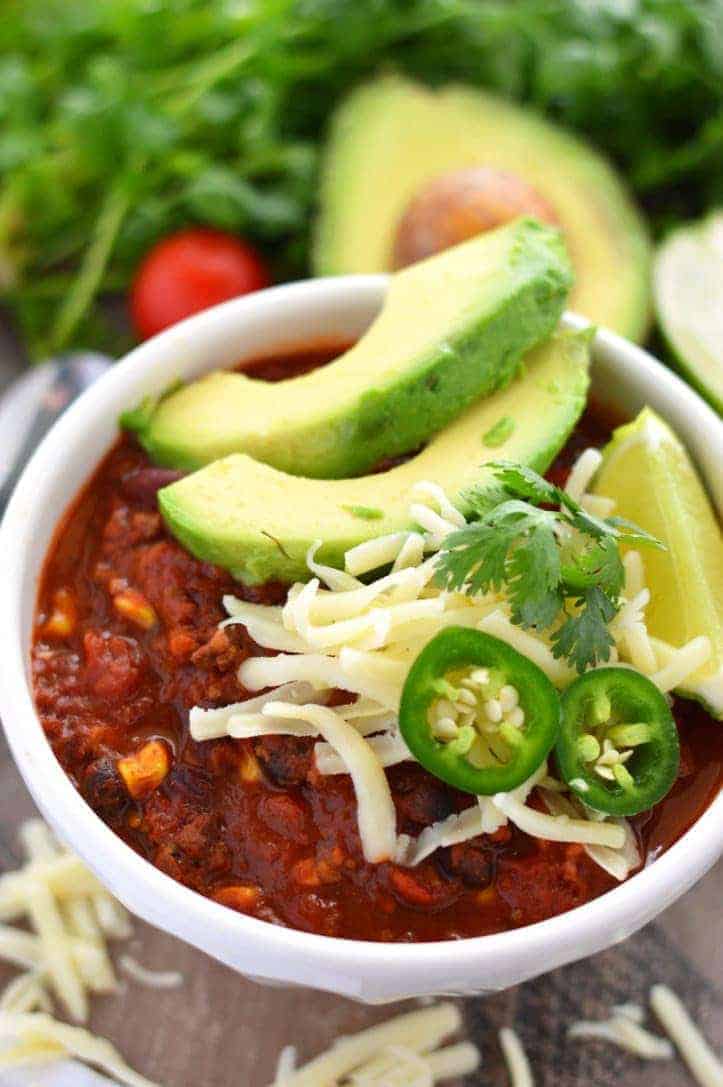 closeup of homemade chilli with cheese and avocado slices on top