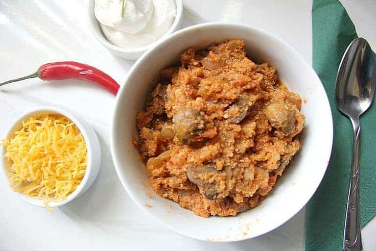 cauliflower homemade chilli in a white bowl next to a bowl of cheese