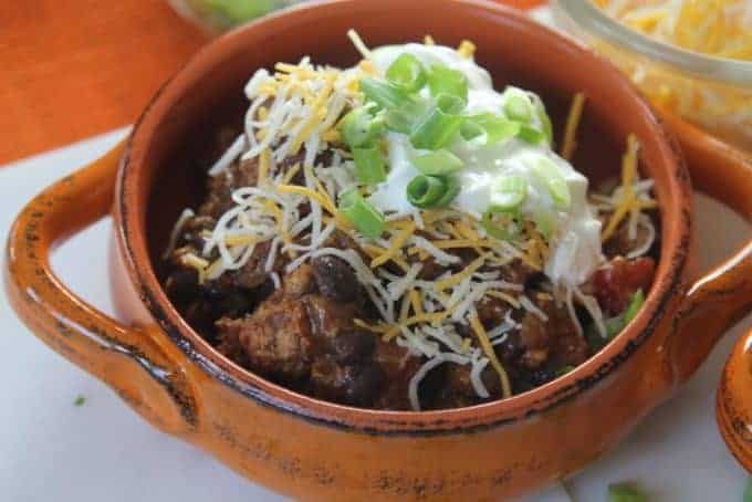 closeup of homemade chilli in orange bowl with sour cream on top