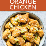 overhead view of a bowl of orange chicken garnished with green onions.