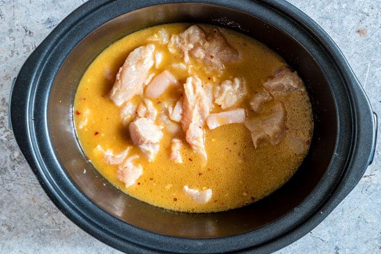slow cooker containing orange chicken raw chicken and orange chicken sauce