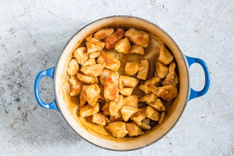 orange chicken in a pot with blue handles on a countertop