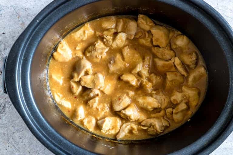 inside of a slow cooker crock containing orange chicken sauce and orange chicken