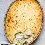 A fish pie with some scooped out with spoon and some fish on a table