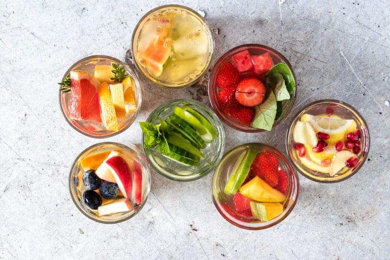 top down shot of 7 glasses of fruit infused water with various fruit