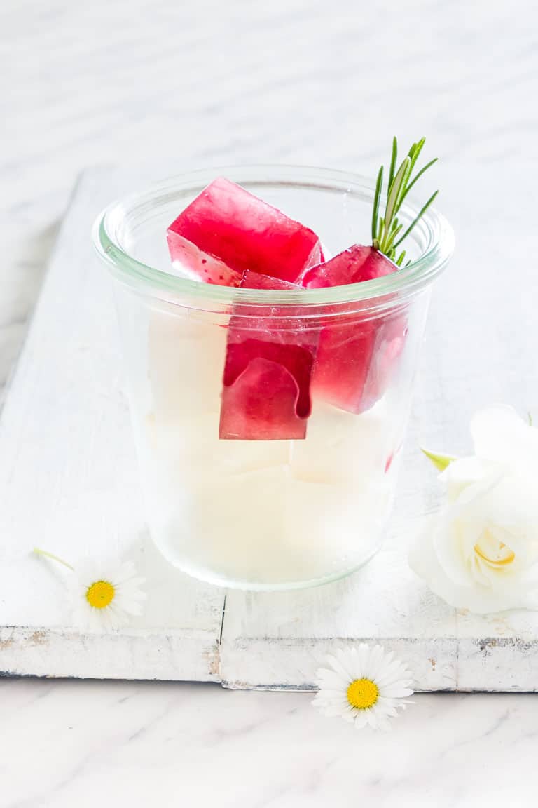 Infused water ice cubes in a glass with water and rosemary garnish