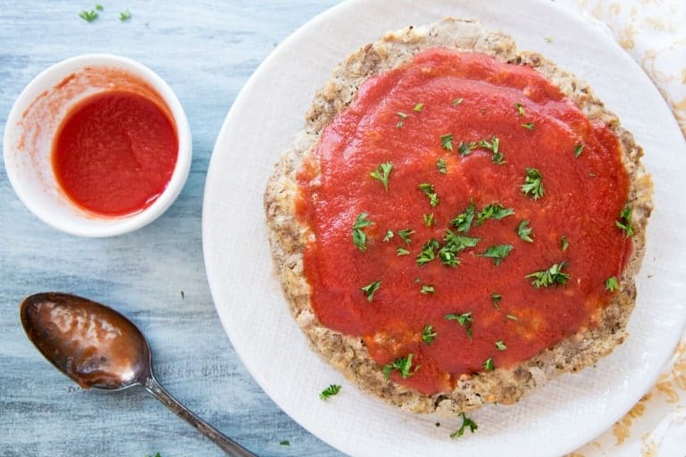 instant pot meatloaf topped with tomato sauce next to a white bowl of sauce