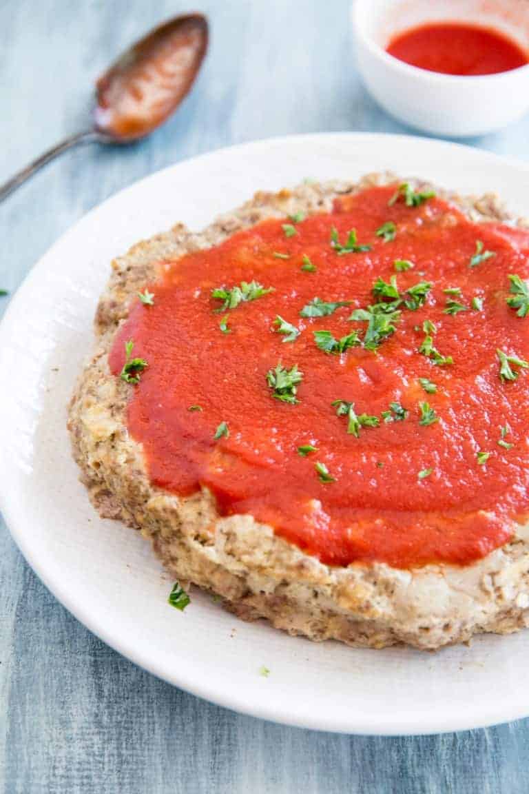 closeup of instant pot meatloaf whole on a white plate with tomato sauce on top