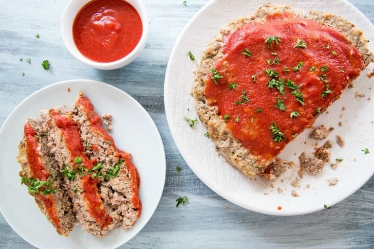 overhead view of instant pot meat loaf on white plates next to tomato sauce cup
