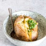 An instant pot baked potato in a bowl with some butter and a spoon