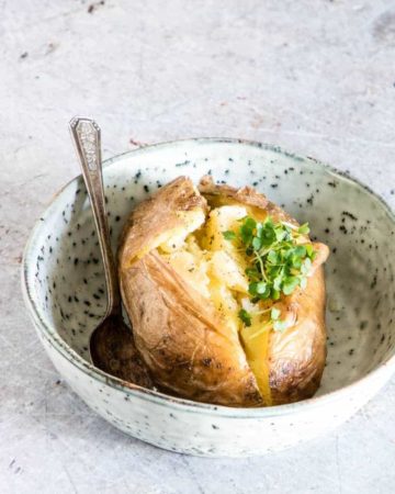 An instant pot baked potato in a bowl with some butter and a spoon