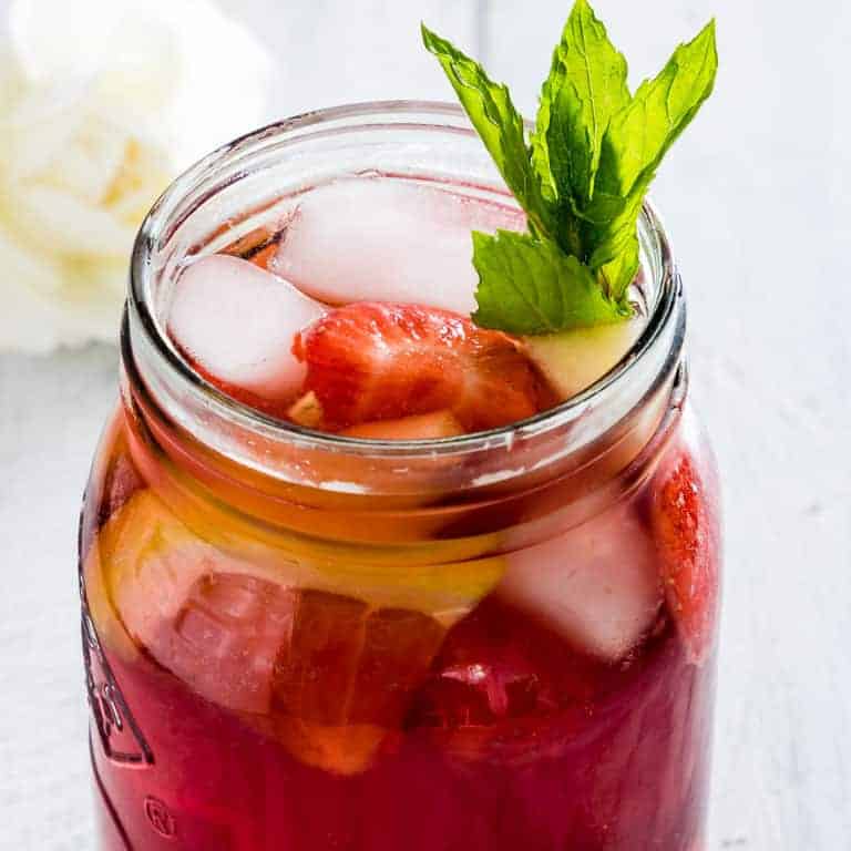 a glass of sangria mocktail garnished with fruit, ice and mint