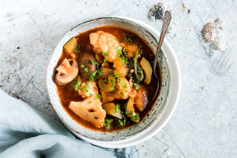 Horizontal image of low carb vegetable soup with garnish and a spoon