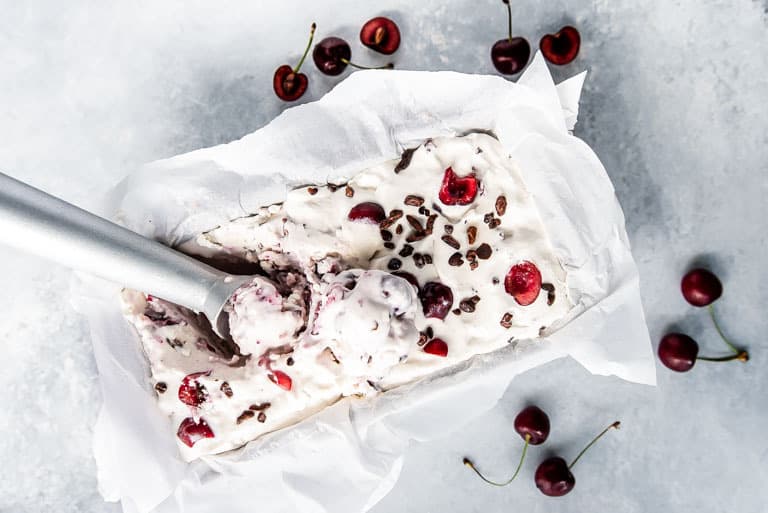 Landscape image of no churn low carb ice cream with cherries and cocoa nibs with an ice cream scoop