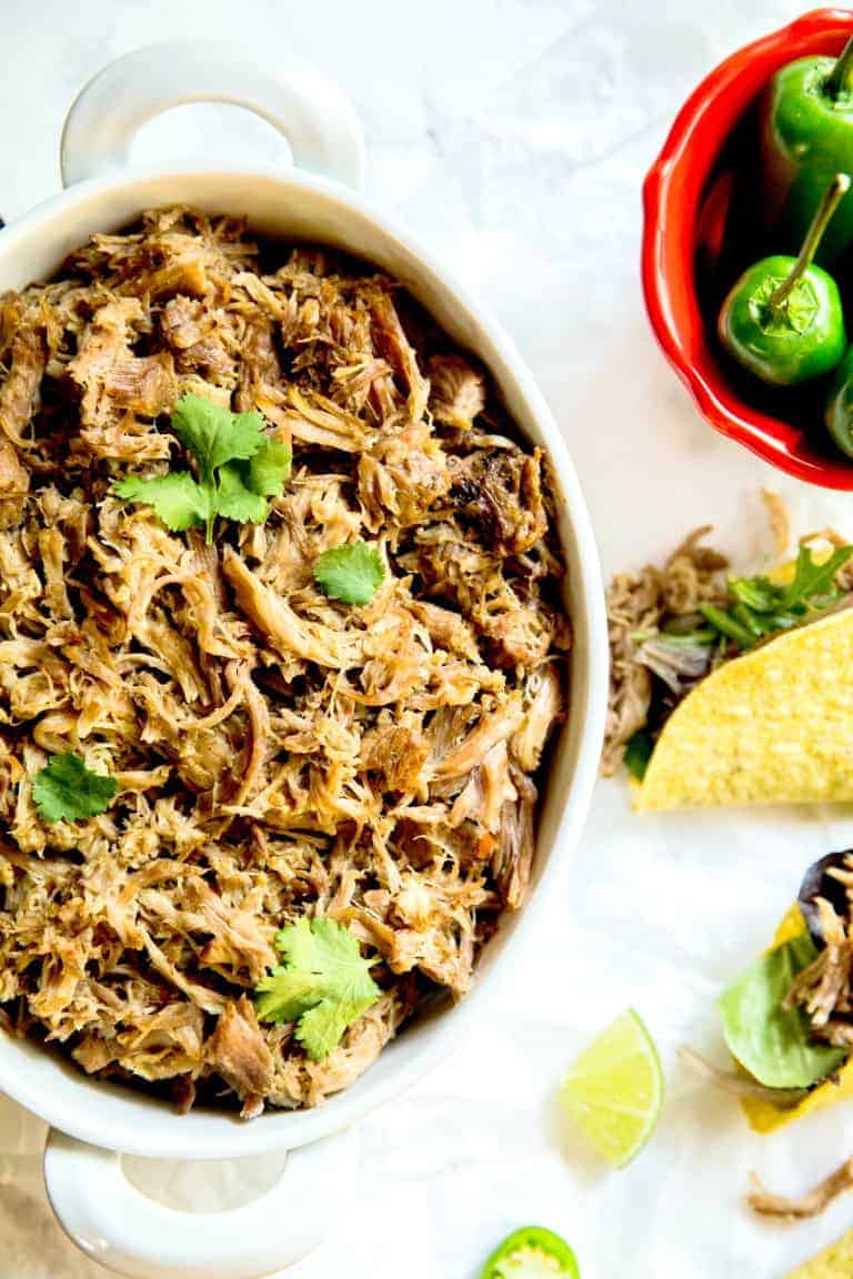 instant pot pulled pork in a large white bowl next to tacos and peppers