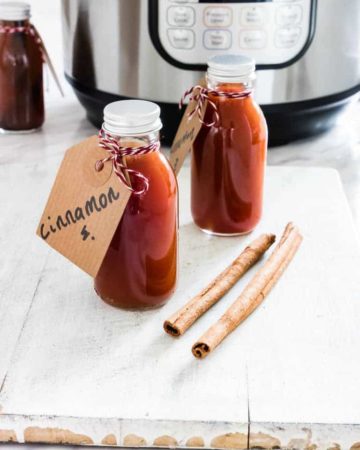 Two gifting bottles filled with Instant Pot Cinnamon Extract tied with a handwritten label set in front of the Instant Pot