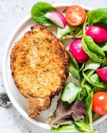 One serving of Air Fryer Pork Chops on a white dinner plate served with fresh greens and tomato salad