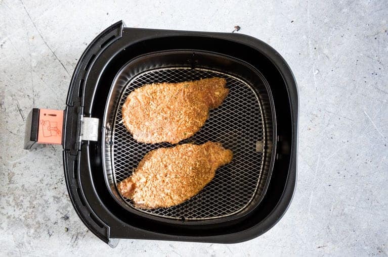 Two coated Air Fryer Pork Chops in the air fryer basket ready to be cooked