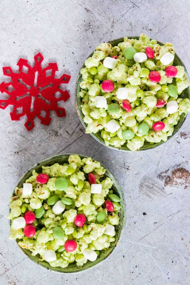 top down view of two ceramic bowls filled with Grinch Popcorn on a countertop and set next to a festive red snowflake coaster