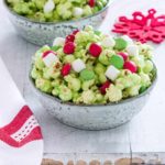 two ceramic bowls filled with Grinch Popcorn on a wooden table next to red print cloth napkin and festive red snowflake coaster