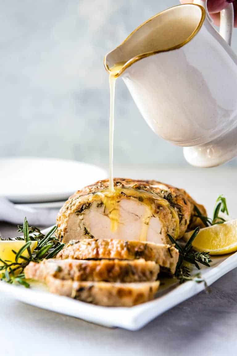 Garlic Butter Gravy being poured onto the Instant Pot Turkey Breast that is sliced and ready to serve on a white platter